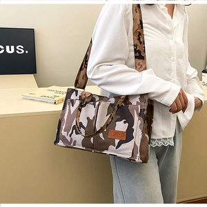 Detail view of large camo tote bag with adjustable wide strap and brown leather logo tag