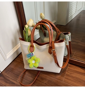 Détail du sac fourre-tout tissé crème avec anses en cuir marron et pendentif fleur