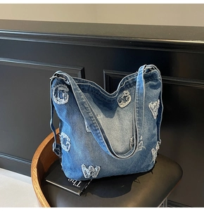 Close-up of washed denim tote bag showing distressed ripped letter texture and fringe detail