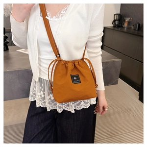 Detail showing the brown drawstring bucket bag with branded label and long shoulder strap