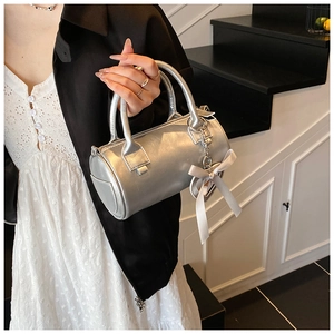 Dettaglio di una borsa a cilindro argento con ciondolo a cuore e fiocco indossata