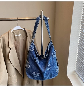 Detailed view of blue denim hobo bag with vintage letter patchwork and frayed embroidery