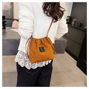 Close-up of caramel drawstring bucket bag with black label showing the casual crossbody style