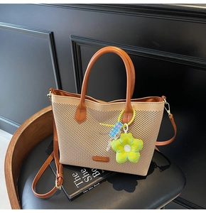 Détail du sac cabas tissé beige avec anses en cuir marron et pendentif fleur verte