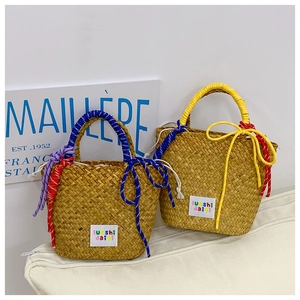 Detail of colorful woven handles and ribbon bows on handmade straw tote bags