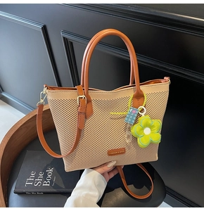Détail d'un sac fourre-tout tissé beige avec anses en cuir marron et breloque fleur verte