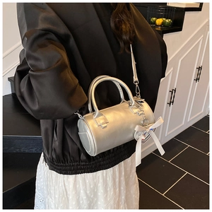 Silver metallic cylinder bag with white ribbon bow and chain strap shown on model