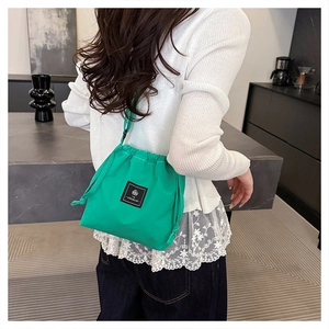 Detail of bright green drawstring bucket bag with black leather logo patch on nylon fabric
