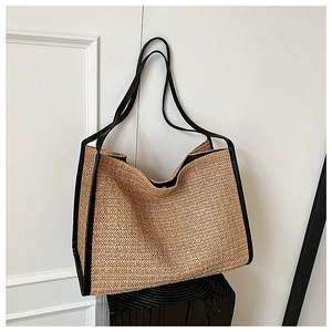 Detail of minimalist woven straw tote bag featuring contrast black leather piping and trim