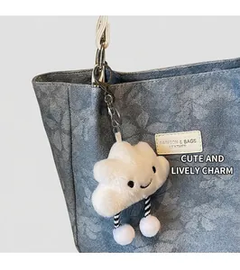Close-up of a white fluffy cloud keychain charm with a smiling face on a denim bag