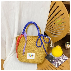 Detail of hand-woven straw tote bag featuring colorful braided rope handles and tassel accents