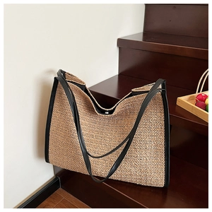 Close-up of woven straw tote bag texture with black leather trim on wooden stairs