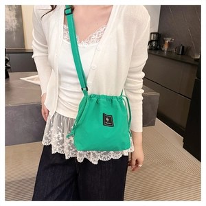 Close-up of green canvas drawstring bucket bag worn with a casual white outfit
