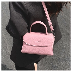 Détail du sac à bandoulière en cuir rose avec ferrures argentées sur blazer gris