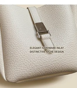 Detail of creamy white litchi grain leather texture and silver metal lock on bucket bag