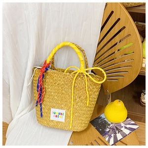 Detail of hand-woven straw basket bag with a bright yellow bow and colorful charm