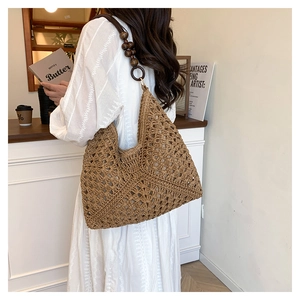 Close-up of bohemian brown straw shoulder bag featuring wooden bead straps and hollow weave