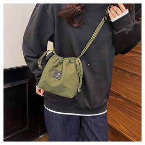 Olive green drawstring bucket bag with adjustable strap worn by model on stairs