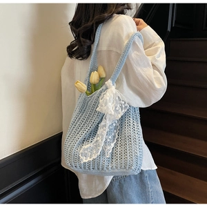 Detailed close-up of light blue knitted tote bag featuring a white lace bow decoration