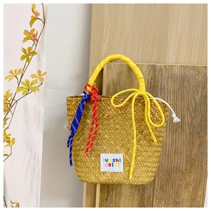 Detailed close-up of woven straw handbag with yellow bow handles and colorful rope accents