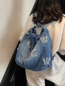 Retro blue denim tote bag with frayed G and W lettering worn by model in minimalist setting