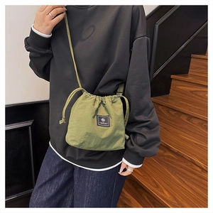 Detail of olive green drawstring crossbody bucket bag with black woven label on model