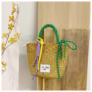 Detail of woven straw handbag with vibrant green handles and colorful knot accents