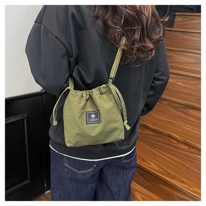 Detail of green nylon drawstring crossbody bag with logo patch and wrinkled texture