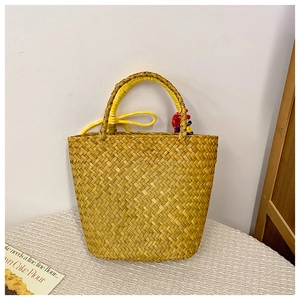 Detail of hand-woven straw basket bag with yellow handles and colorful rope ornament