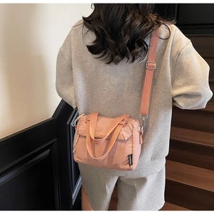 Model wearing pink nylon crossbody bag with adjustable strap on a minimalist staircase