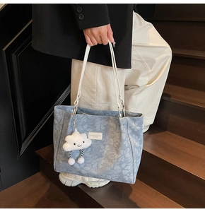 Détail du sac cabas en denim floral avec étiquette en cuir blanc et breloque peluche