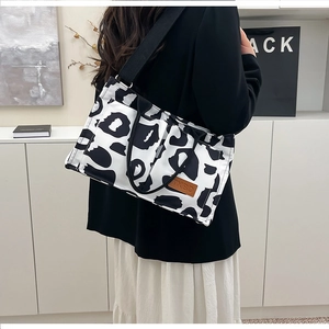 Detail of the cow print canvas tote bag featuring a leather logo patch and wide strap