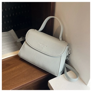 Détail du sac bandoulière bleu clair avec texture litchi et logo en cuir tendance
