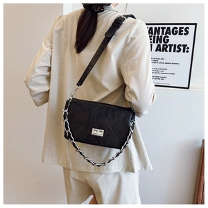 Detail of black quilted leather shoulder bag with silver chain strap on a model