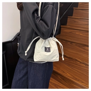 Detail of cream drawstring bucket bag with black logo patch and slim shoulder strap