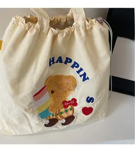 Detail of off-white canvas tote bag featuring embroidered bear and drawstring closure