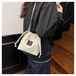Close-up of cream canvas drawstring bucket bag with black brand patch on model