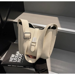 Détail du sac seau en cuir grainé blanc crème sur des livres avec fermoir en métal argenté