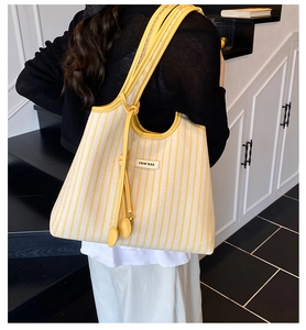 Detail of yellow and white striped canvas tote bag with leather straps on model shoulder