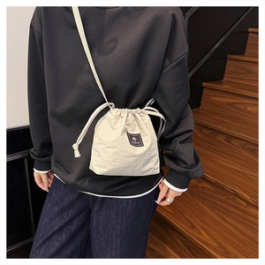 Detail of minimalist cream drawstring bucket bag with micro-wrinkle fabric and strap