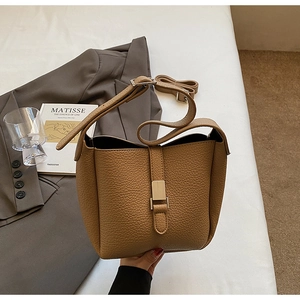 Détail du sac seau en cuir camel avec fermoir doré sur un fond minimaliste chic
