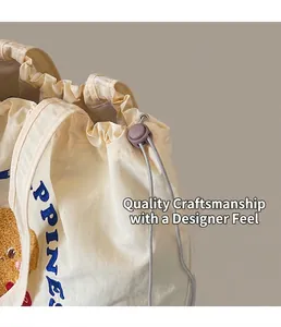 Detail of off-white tote bag featuring blue HAPPINESS embroidery and a brown bear patch