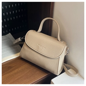 Détail du sac en cuir litchi crème avec logo embossé sur une surface en bois