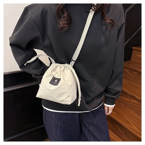 Close-up of minimalist cream drawstring bucket bag worn by model in casual urban setting