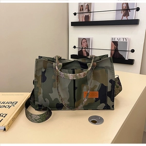 Detail of camouflage canvas tote bag featuring brown leather logo patch and metal hardware