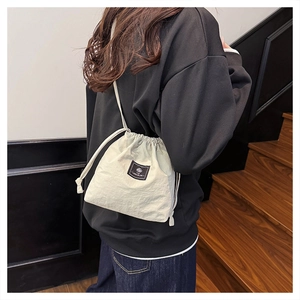 Detail of a beige drawstring bucket bag with black logo tag worn by a model
