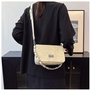 Detailed back view of a beige quilted crossbody bag with silver chain on a model