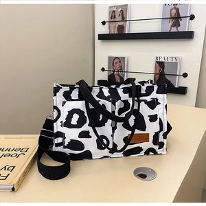 Close-up of cow print canvas tote bag showing front double pockets and leather brand patch