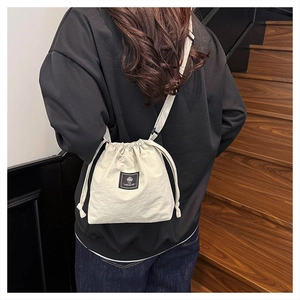 Back view of beige drawstring crossbody bag in nylon fabric on a model in a stairwell