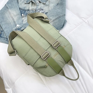 Detail view of light green nylon backpack with silver metal buckles on white bedding